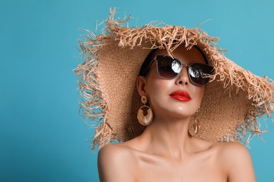Attractive woman in fashionable sunglasses and wicker hat against light blue background. Space for text
