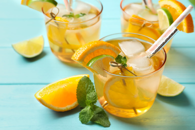 Delicious refreshing drink with orange and lime slices on light blue wooden table, closeup