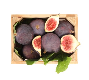 Whole and cut tasty fresh figs with green leaves in wooden crate on white background, top view
