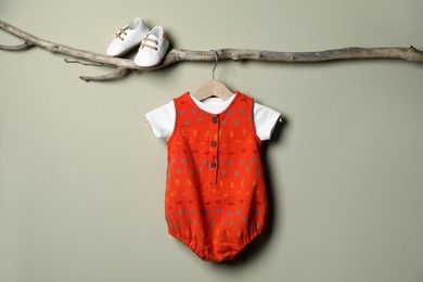 Baby bodysuit and booties on decorative branch near beige wall