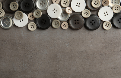 Many plastic sewing buttons on grey background, flat lay. Space for text