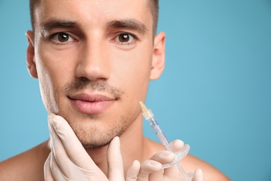 Man getting facial injection on light blue background, closeup. Cosmetic surgery