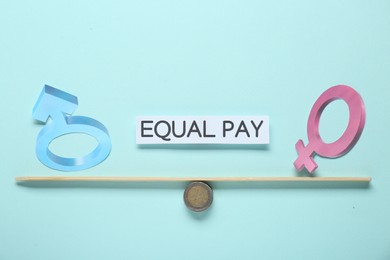 Photo of Equal pay concept. Gender symbols on miniature seesaw against light blue background
