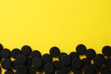 Activated charcoal pills on yellow background, flat lay with space for text. Potent sorbent