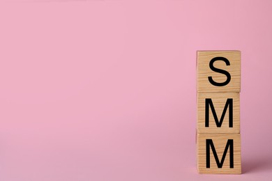 Wooden cubes with abbreviation SMM (Social media marketing) on pink background. Space for text