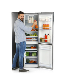 Young man taking juice out of refrigerator on white background