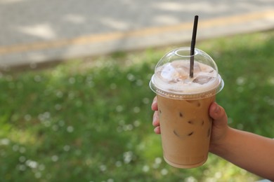 Woman holding plastic takeaway cup of delicious iced coffee outdoors, closeup. Space for text