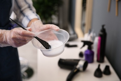 Professional hairdresser holding bowl with hair dye in beauty salon, closeup