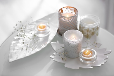 Burning candles in beautiful holders and flowers on table indoors
