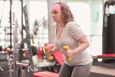Overweight woman training with dumbbells in gym