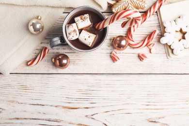 Flat lay composition with cup of tasty cocoa and Christmas candy canes on white wooden table, flat lay. Space for text