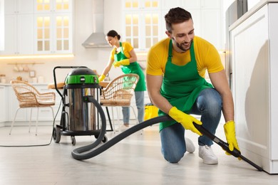 Professional janitor in uniform vacuuming floor indoors