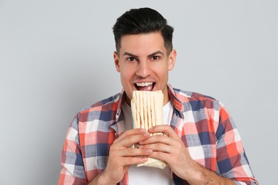 Photo of Man eating delicious shawarma on grey background