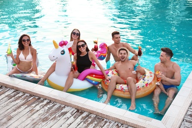 Happy young friends with refreshing cocktails relaxing in swimming pool