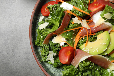 Delicious kale salad with prosciutto served on grey table, top view