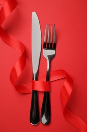 Photo of Cutlery set with ribbon on red background, flat lay. Romantic table setting