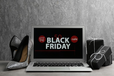 Laptop with Black Friday announcement, shoes and gifts on table against grey background