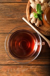Photo of Cup of delicious ginger tea and honey on wooden table, flat lay