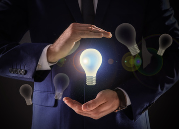 Image of Idea concept. Businessman demonstrating glowing light bulb on dark background, closeup