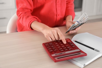 Woman counting money with calculator at table, closeup