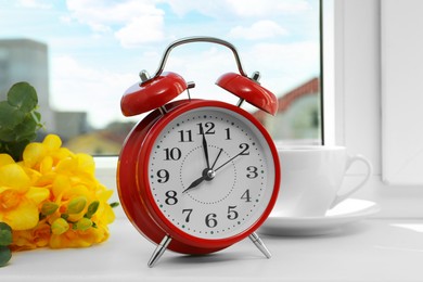 Alarm clock, beautiful yellow freesias and cup of drink on windowsill. Good morning