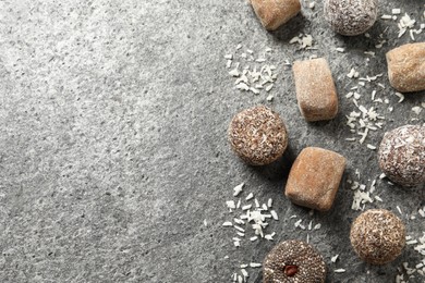 Different delicious vegan candy balls and desiccated coconut on grey table, flat lay. Space for text