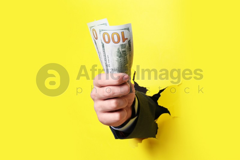 Photo of Businessman breaking through yellow paper with money in fist, closeup