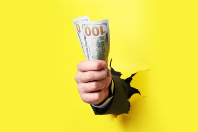 Businessman breaking through yellow paper with money in fist, closeup