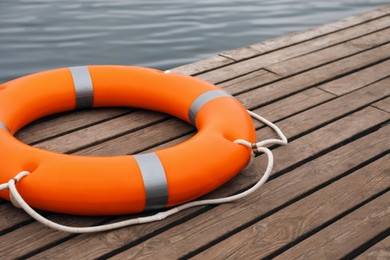 Orange lifebuoy on wooden pier near water. Rescue equipment