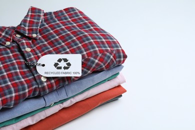 Stack of clothes with recycling label on white background, space for text
