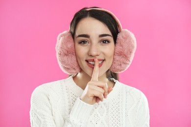 Beautiful young woman wearing earmuffs on pink background