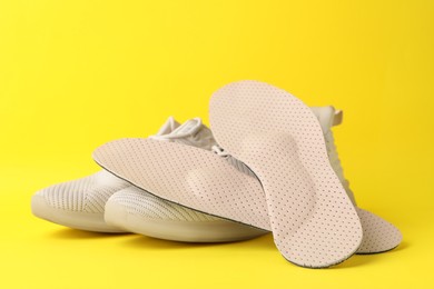 Beige orthopedic insoles and shoes on yellow background