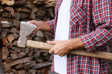 Man with sharp ax near wood pile outdoors, closeup