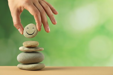 Woman putting stone with drawn happy face onto stack against blurred background, closeup and space for text. Zen concept