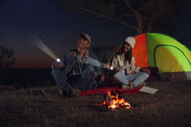 Couple with flashlights near bonfire at night. Camping season