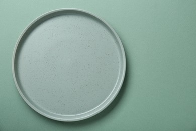 Photo of Empty ceramic plate on green background, top view. Space for text