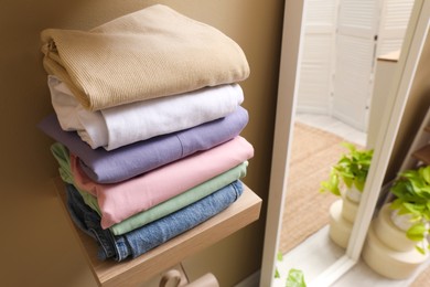 Photo of Wooden shelf with stacked clothes on beige wall near mirror. Dressing room interior