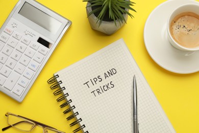 Flat lay composition with phrase Travel Tips written in notebook, cup of coffee, calculator and plant on yellow background