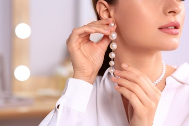 Young woman trying on elegant pearl earring indoors, closeup. Space for text