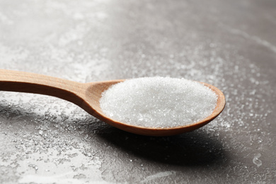 Photo of Spoon of white sugar on marble table, closeup