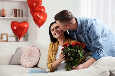 Photo of Boyfriend presenting beautiful bouquet of roses to his girlfriend in room decorated with heart shaped balloons. Valentine's day celebration
