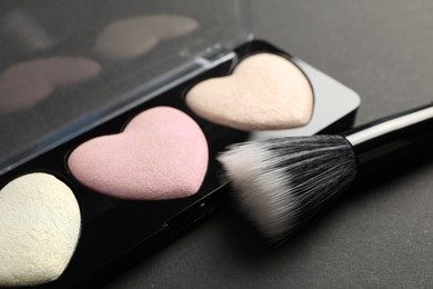 Palette of heart shaped eyeshadows with brush on dark background, closeup