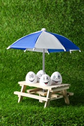 Eggs with drawn happy faces, small picnic table and umbrella on green grass