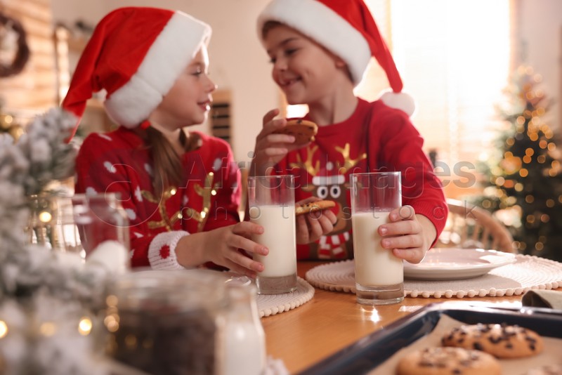 Photo of Cute little children with delicious Christmas cookies and milk at home, focus on hands