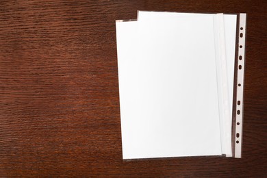 Photo of Punched pockets with paper sheets on wooden table, flat lay. Space for text
