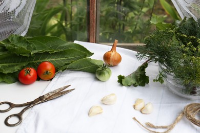 Fresh green herbs, tomatoes, garlic cloves, onion, scissors and twine on table indoors