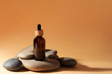 Bottle of face serum and spa stones on beige background, space for text