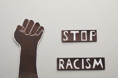 Phrase Stop Racism near paper hand with clenched fist on light background, flat lay