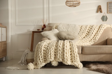 Photo of Cozy living room interior with beige sofa, knitted blanket and cushions
