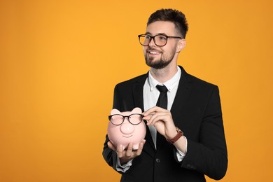 Happy businessman with piggy bank on orange background. Space for text